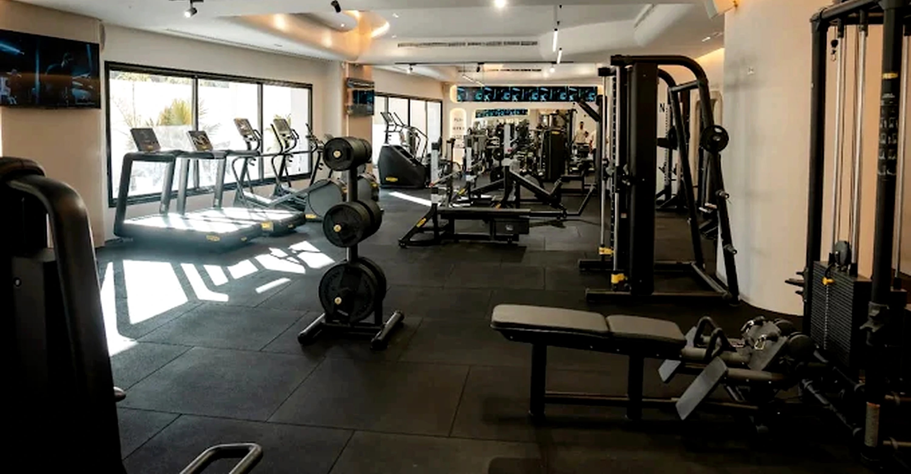 A wide view across the training floor at Naouar Prestige Gym, showing resistance machines, free weights and the cardio zone under daylight.