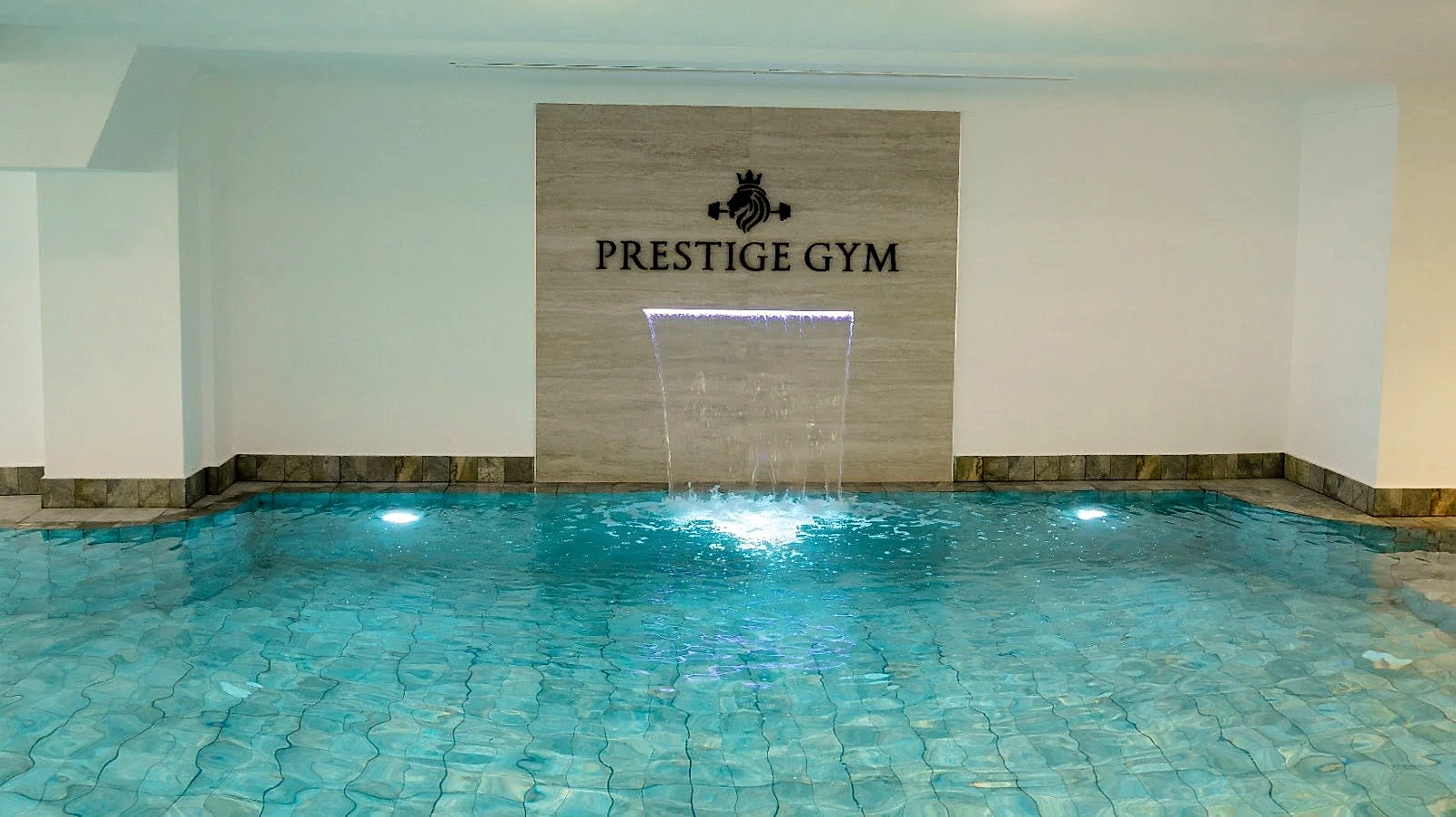 The indoor swimming pool at Naouar Prestige Gym, lit from beneath, with a sheet water feature falling into it.